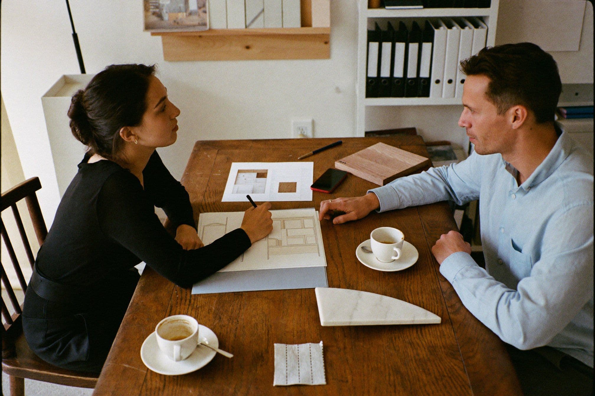 Interior designer sketching a room layout while a homeowner points at the floor plan in a first one-to-one meeting.