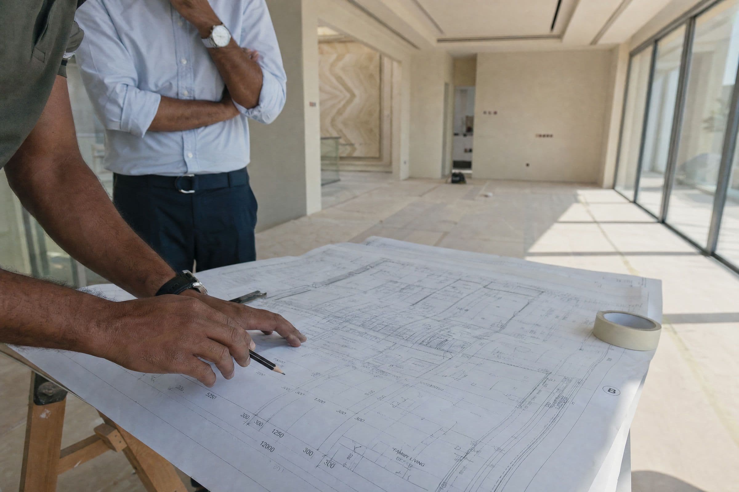 A large drawing on a trestle table being checked on site, with the unfinished room behind